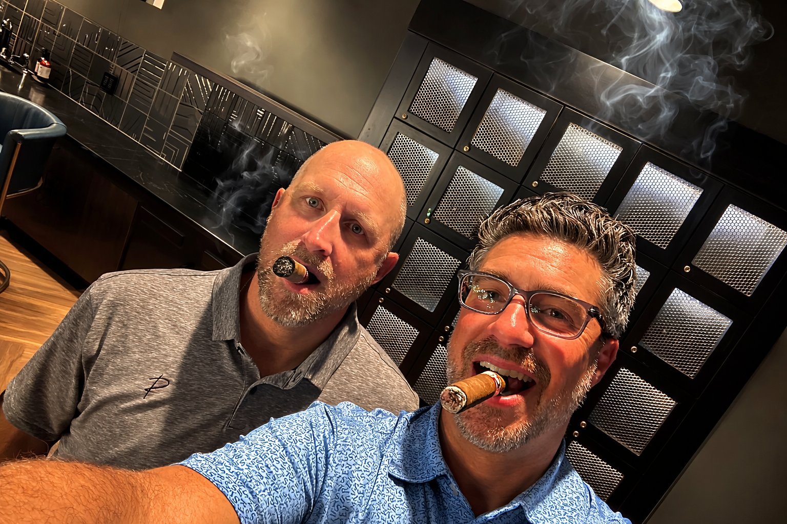 Joe Clark and Patrick Malloy celebrating with cigars in the C-Suite Lounge in front of the bourbon lockers, Revelance grand opening 2024