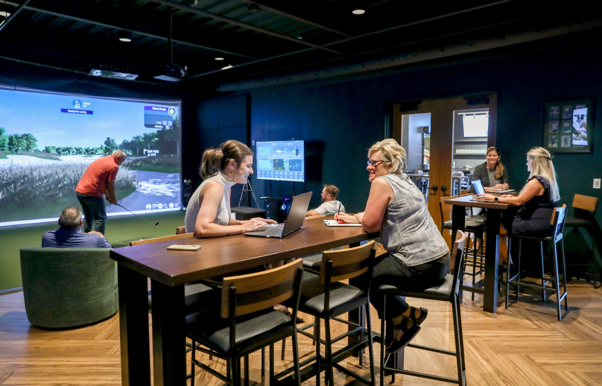 Team working at high-top tables while a colleague hits on the golf simulator at Emergency 9, Revelance Mason Ohio